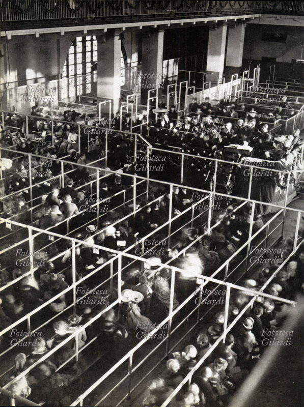 EMIGRAZIONE Immigranti appena sbarcati a New York, in attesa nella sala principale di Ellis Island di essere registrati, ammessi alla visita medica e di ricevere i documenti. Fotografia di anonimo. Stati Uniti d\