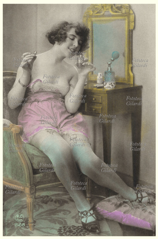 PROFUMO Giovane donna in sottoveste, si profuma alla toeletta. Annusa delicatamente la boccetta di essenza profumata. Cartolina postale, primi circa 1910