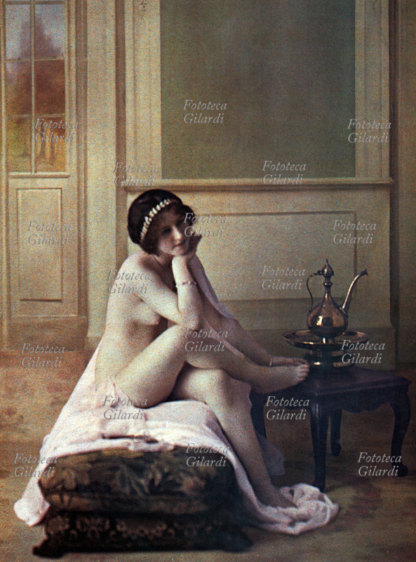 EROS Giovane donna seduta su un sofa con gamba accavallata, a destra una ampolla di stile orientale. Autocromia a tema erotico di Edmond Goldschmidt, circa 1892
