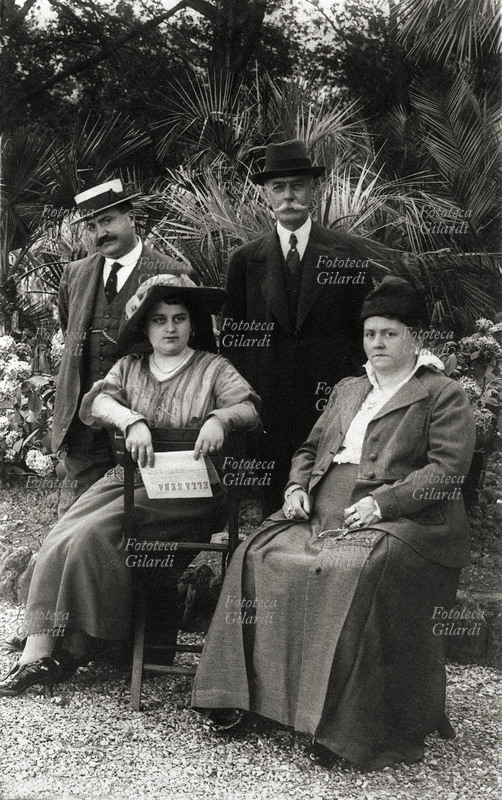 MODA 1900 Due coppie eleganti posano in giardino, le signore sono sedute, gli uomini posano in piedi alle loro spalle. Una signora ha in mano il giornale quotidiano \