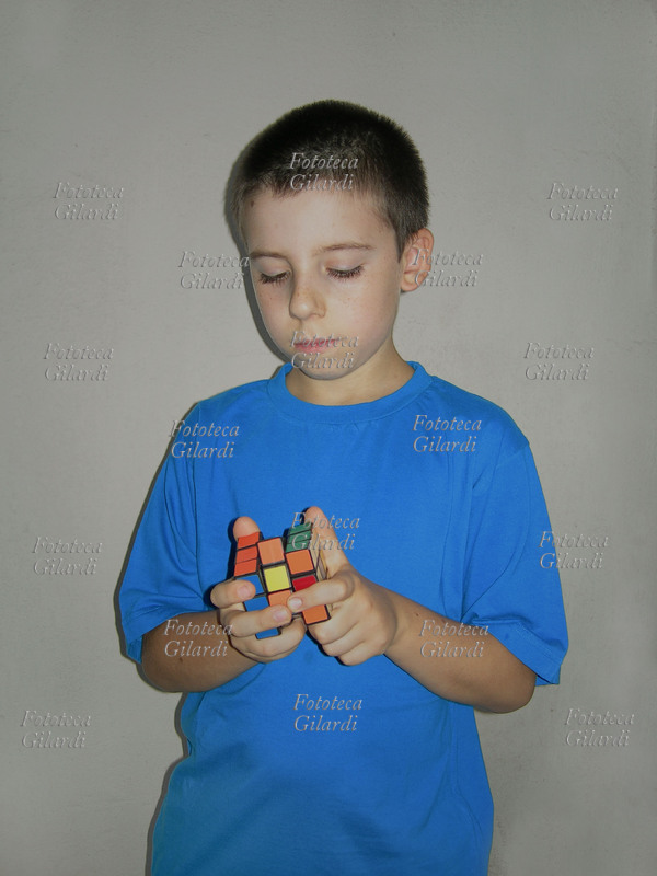 GIOCHI Bambino tenta di risolvere il Cubo di Rubik, un rompicapo inventato dal professore di architettura e scultore ungherese Ernö Rubik nel 1974. Lo scopo del gioco è di risalire alla posizione originale dei 26 cubetti portando il cubo ad avere per ogni faccia un unico colore. Il cubo può assumere ben 43.252.003.274.489.856.000 combinazioni diverse, solo una delle quali è quella corretta. Il gioco divenne molto diffuso e popolare, la stima delle vendite nel 1982 superava i 100 milioni di pezzi.