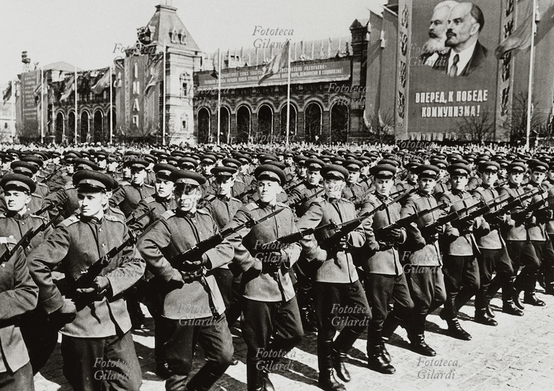 URSS 1960 Mosca: celebrazione del primo maggio sulla Piazza Rossa. Lungo le mura del Cremlino, sotto un grande stendardo con i ritratti di Marx e Lenin sfila un battaglione di soldati con baionetta.