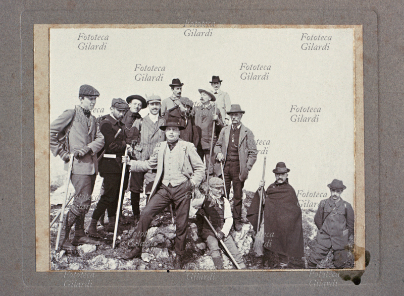MONTAGNA gruppo di escursionisti con equipaggiamento sportivo, in posa insieme ad altri abbigliati elegantemente (personaggi importanti?), forse all\