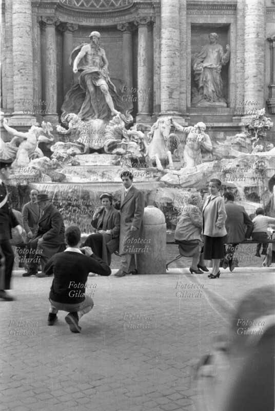 TURISMO in posa dinnanzi alla fontana di Trevi a Roma per la classica foto ricordo, il fotografo si accoscia per una migliore inquadratura. Fotografia di Ando Gilardi (1921 - 2012) #andogilardi, Roma 1950 circa.