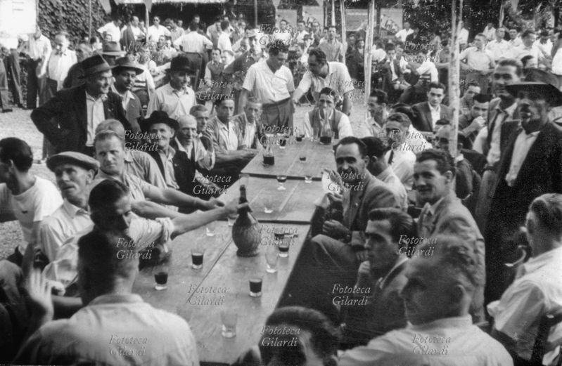 VINO bellissima foto ricordo di un gruppo ad una sagra. Veduta della tavolata: al centro si trova un fiasco di vino. Italia, 1950 circa.