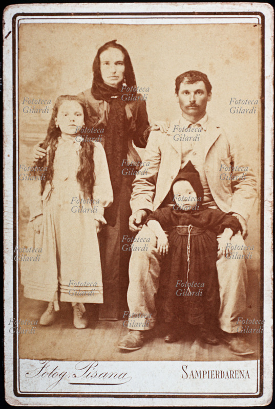 FAMIGLIA genitori in posa con i due figli, un maschio e una femmina. Il padre è seduto e tiene tra le ginocchia il bimbo, vestito da piccolo frate, forse per un voto. La madre è in piedi, vestita di scuro e a capo coperto, tiene una mano sulla spalla della figlia, già grande. Fotografia eseguita in atelier \