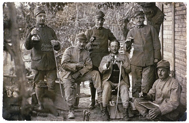 VINO Sei militari in un momento di tregua bevono alla salute. Tre sono seduti (uno in terra) e tre sono in piedi; sullo sfondo si vede una vigna dalla quale è stato probabilmente prodotto il vino che stanno gustando. Italia, 1914 ca.