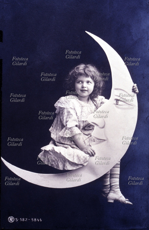 BAMBINA in posa, seduta sulla falce di Luna, guarda lateralmente. Allestimento in atelier, fotografia viraggio seppia, Italia 1905.