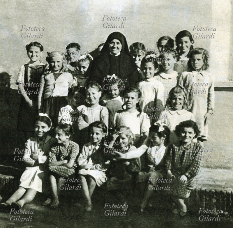 RELIGIONE Suora della congregazione delle Sorelle dei Poveri di Santa Caterina da Siena in posa sorridente in mezzo alle bambine del doposcuola, Roma 1948. La congregazione fu fondata dalla Beata Savina Petrilli (1851-1923), con la finalità di offrire assistenza morale e materiale alla classe povera e operaia. Nelle sue opere si conta l\
